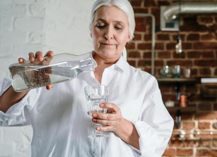 Eine ältere Frau schenkt sich ein Glas Wasser ein
